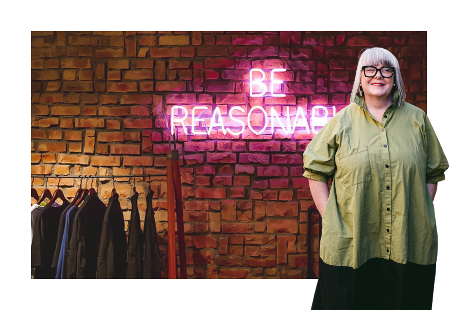 Pictured, Anthea Taylor standing in front of a stock picture of a brick wall with neon lights lit up in pink saying "be reasonable"