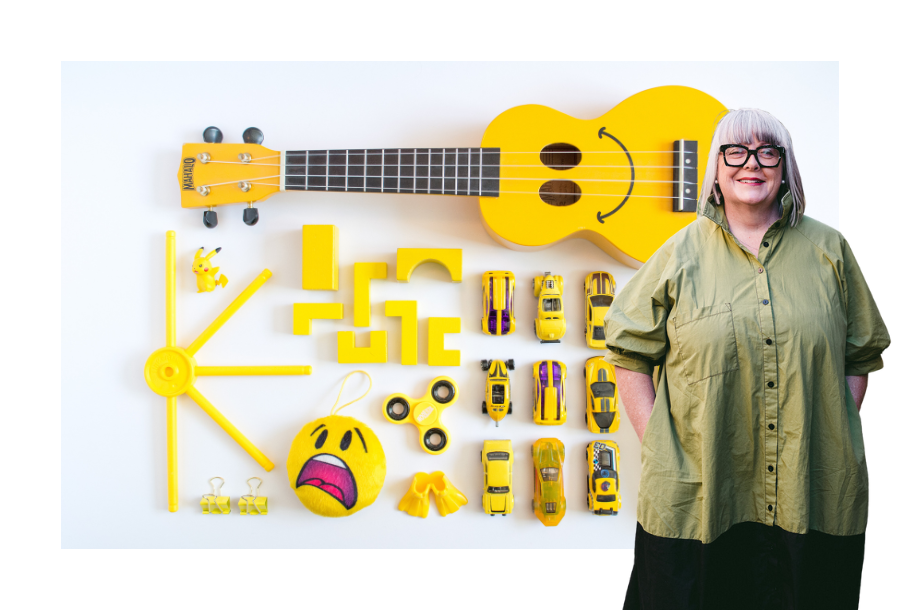 Pictured: Anthea Taylor standing in front of a stock picture of bright yellow toys all organised neatly in a flat-lay.
