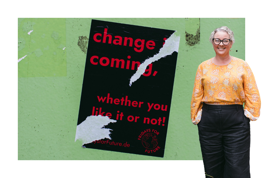 Pictured, Amy Osborne, standing in an orange long sleeve top and black trousers. Behind her is an image of a ripped sign that says "Change is coming".