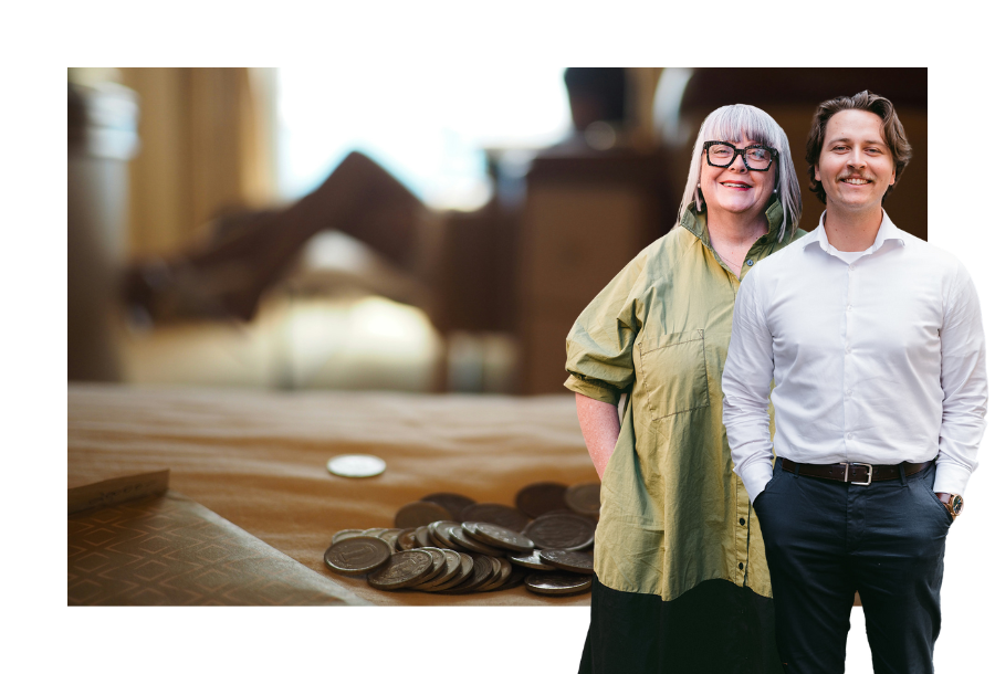 Pictured: Anthea Taylor and Zach Henderson standing smiling towards the camera, behind them is an image of coins laid out on a bed with someone sitting in a chair with their legs up in the background out of focus.